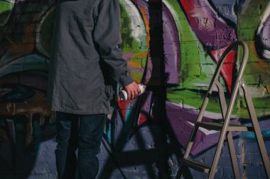 cropped view of street artist painting graffiti with aerosol paint on wall at night clipart