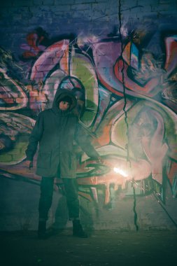 man holding smoke bomb and standing against wall with graffiti at night clipart