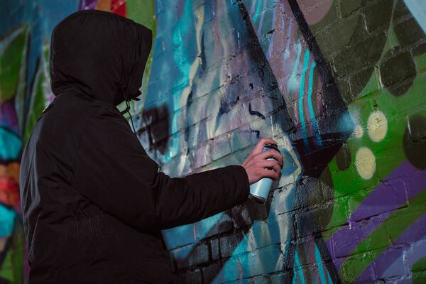 anonymous painting graffiti with aerosol paint on wall at night