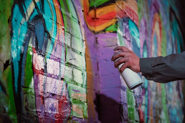 cropped view of street artist painting graffiti with aerosol paint on wall at night