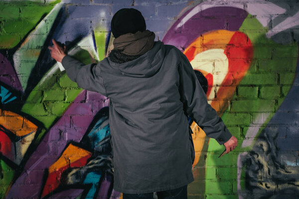 back view of man painting graffiti with aerosol paint on wall at night