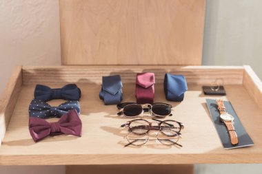 bow ties, neckties, glasses and wristwatch laying on wooden display at shop  clipart