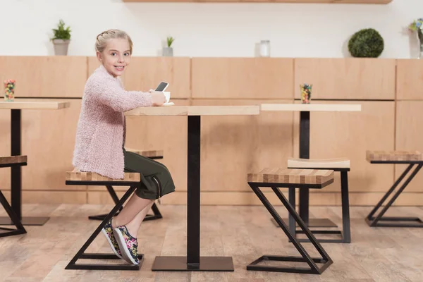 Criança Sorridente Sentada Mesa Com Smartphone Olhando Para Câmera — Fotografia de Stock Grátis