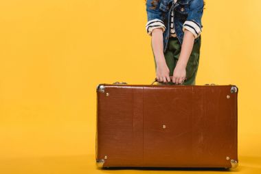partial view of child holding leather suitcase isolated on yellow