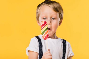 selective focus of adorable little boy with lollipop in hand isolated on yellow clipart