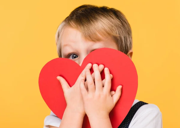 のバレンタインデーのコンセプトを黄色の分離された赤い紙の心と顔を覆っている少年の隠れたビュー — ストック写真
