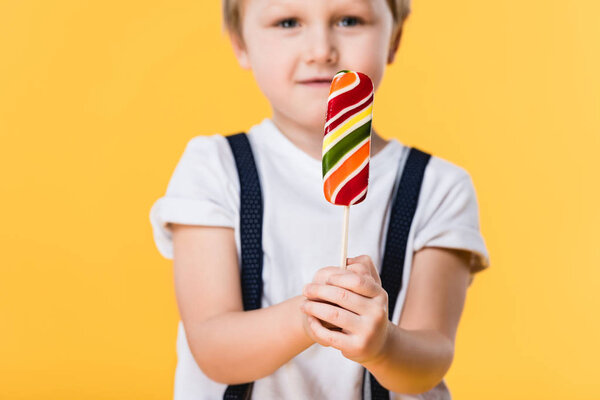selective focus of adorable little boy with lollipop in hand isolated on yellow