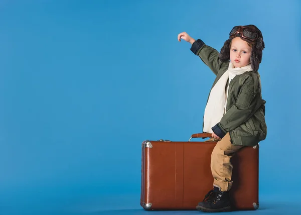男孩在飞行员服装的侧面图坐在蓝色的手提箱隔离 — 图库照片