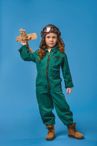 adorable child in pilot costume with wooden plane toy isolated on blue