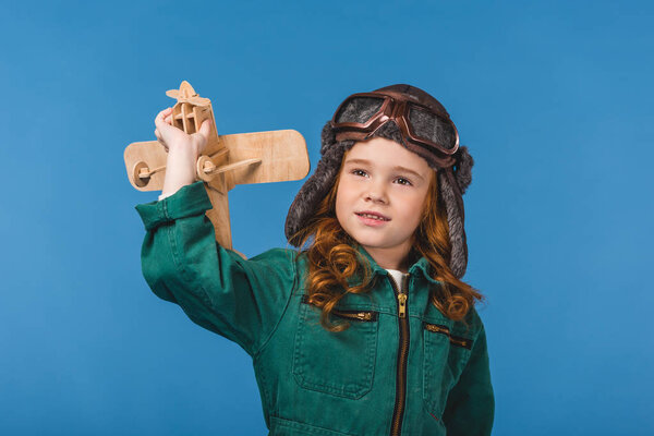 portrait of adorable child in pilot costume with wooden plane toy isolated on blue