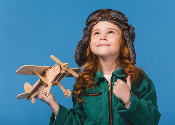 portrait of smiling child in pilot costume with wooden plane toy isolated on blue