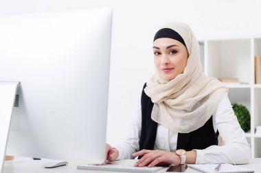 ofiste bilgisayar üzerinde çalışırken kameraya bakarak gülümseyen Müslüman işkadını portresi