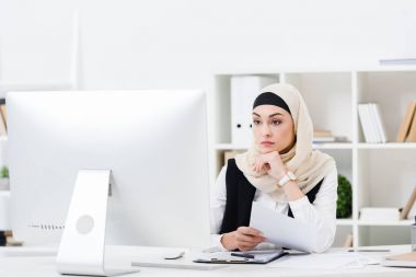 düşünceli Müslüman iş kadını ile işyeri bilgisayar ekranına bakarak kağıtları hijab portresi