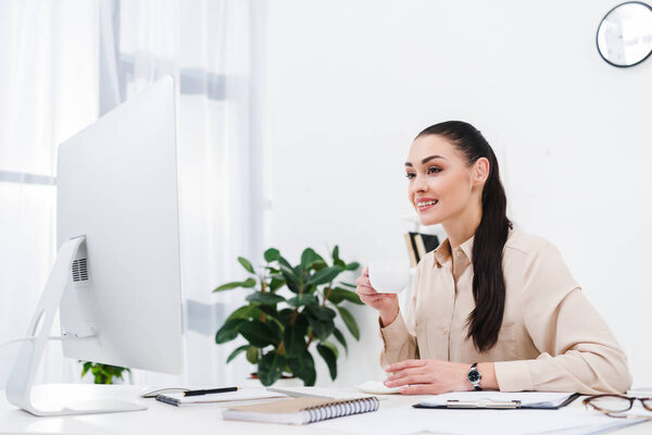 portrait of smiling businesswoman with cup of coffee at workplace in office