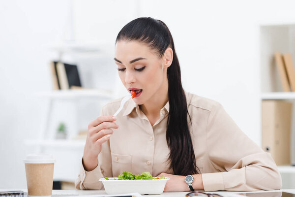 portrait of businesswoman eating take away salad for lunch in office