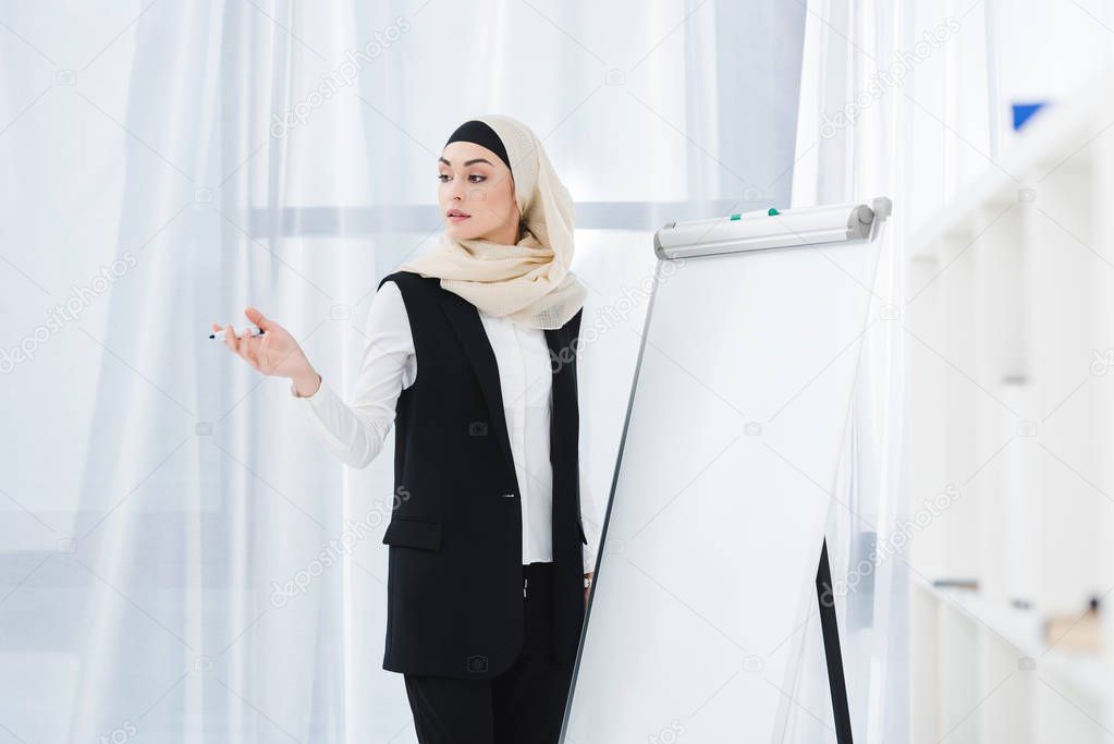 arabic businesswoman in formal wear and hijab standing at white board in office