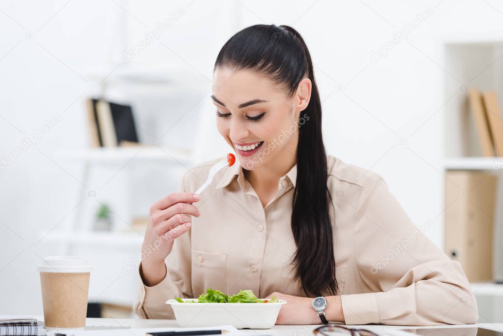 smiling businesswoman eating take away salad for lunch in office