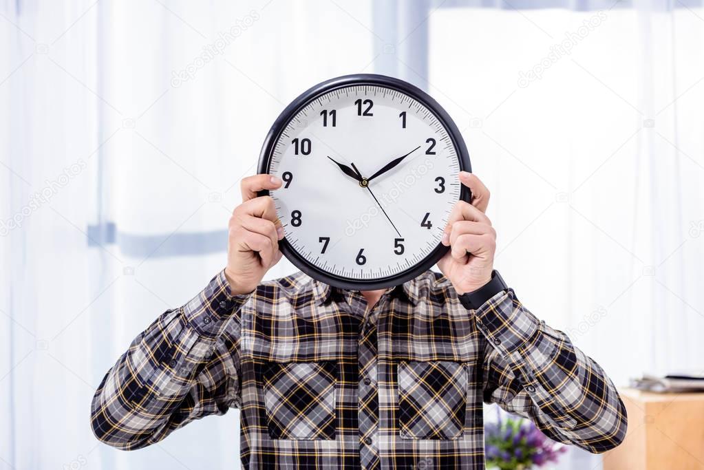 Man holding clock over face in front of window