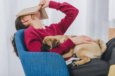 Pretty lady hugging pug and covering her face with book clipart