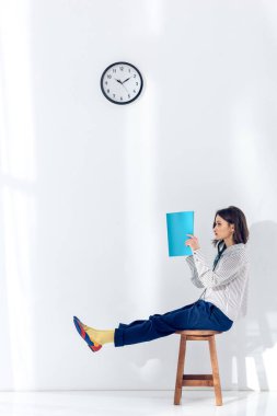 Young woman sitting on chair and reading book under clock clipart