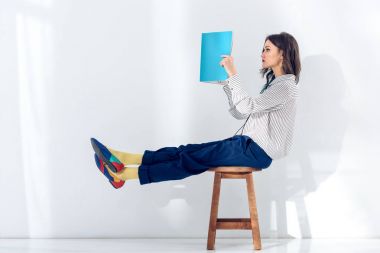 Young woman sitting on chair and reading book clipart