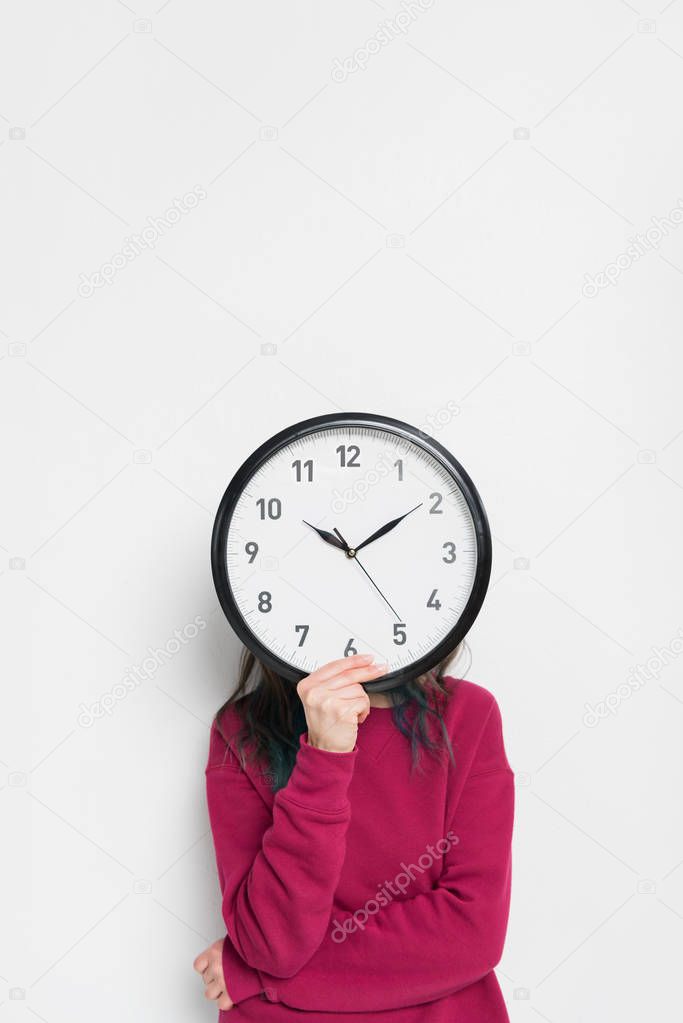 Woman holding clock over her face isolated on white