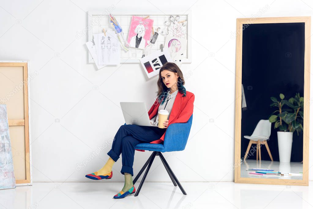 Pretty lady working on laptop and holding coffee cup in light studio
