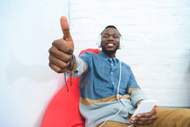 Genç gösteren başparmak kadar akıllı telefon ve kulaklık müzik ile adam