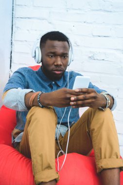 Fasulye çanta içinde otururken smartphone cep telefonu ile müzik dinlerken kulaklık yakışıklı Afrikalı-Amerikalı adam