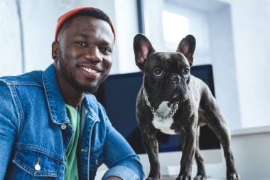 Young man with French bulldog by computer screen clipart