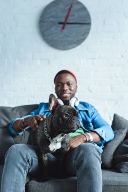 Handsome african american man in headphones cuddling French bulldog clipart