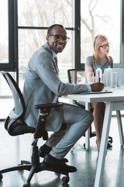 yakışıklı Afrikalı-Amerikalı iş adamı kadın meslektaşı Office ile çalışırken kameraya gülümseyen gözlük