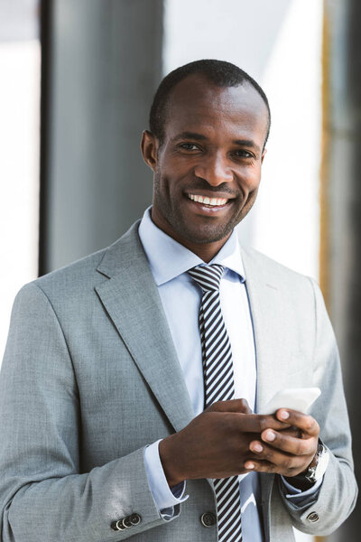 portrait of handsome young african american businessman using smartphone and smiling at camera
