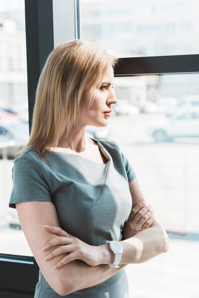 side view of beautiful confident businesswoman standing with crossed arms and looking at window