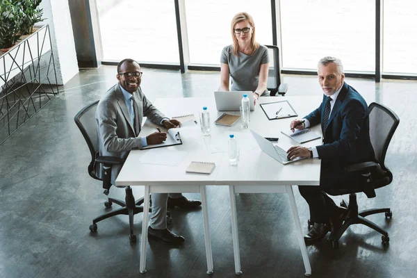 professional multiethnic business people smiling at camera while sitting together at business meeting