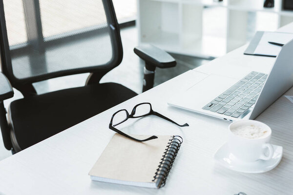 close-up view of eyeglasses, notebook, cup of coffee and laptop on table in office