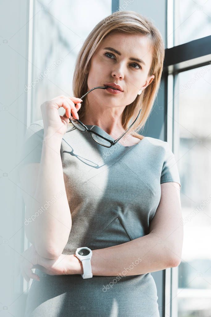 beautiful pensive businesswoman holding eyeglasses and looking away