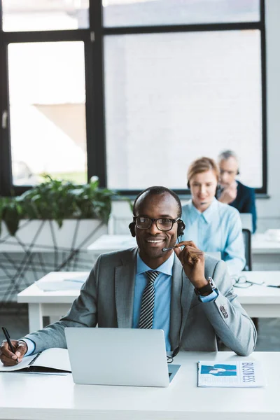 Joven Hombre Negocios Afroamericano Gafas Auriculares Sonriendo Cámara Mientras Trabaja — Foto de Stock