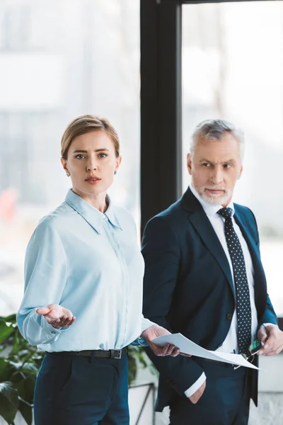 Hombre Negocios Senior Mirando Mujer Negocios Sosteniendo Papeles Mirando Cámara — Foto de stock gratis