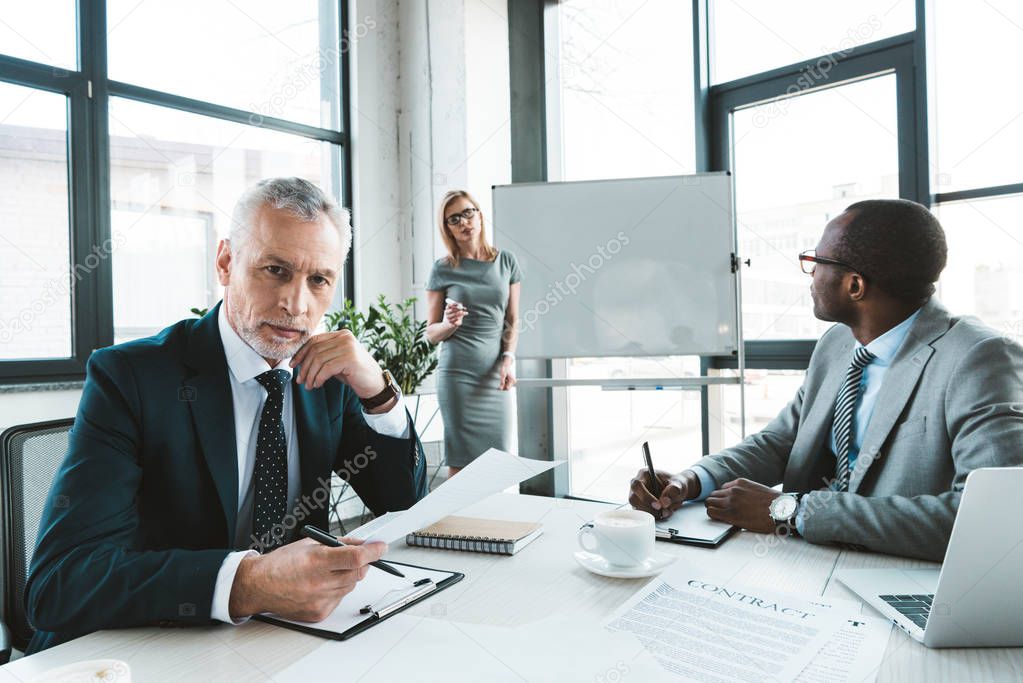 senior businessman looking at camera while having conversation with colleagues at business meeting