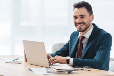 dizüstü bilgisayar kullanarak ve kamera Office gülümseyen yakışıklı genç işadamı