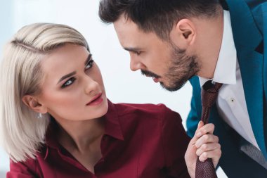 young business people looking at each other while businesswoman holding necktie of handsome businessman clipart