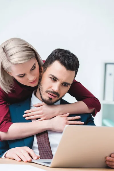 Jovem Mulher Abraçando Bonito Empresário Usando Laptop Escritório — Fotografia de Stock