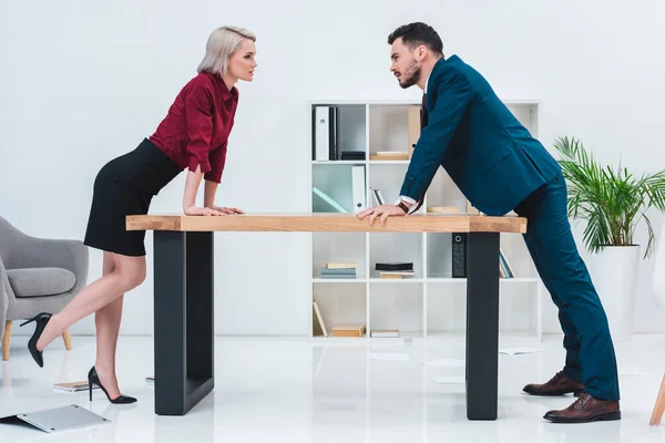 side view of young business people leaning at table and looking at each other in office