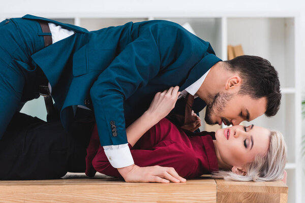 side view of sexy young couple kissing on table in office