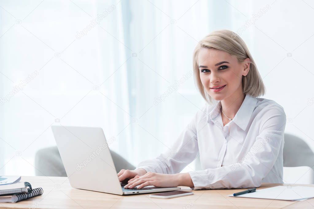 beautiful young businesswoman using laptop and smiling at camera