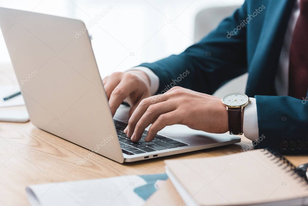 close-up partial view of businessman using laptop at workplace