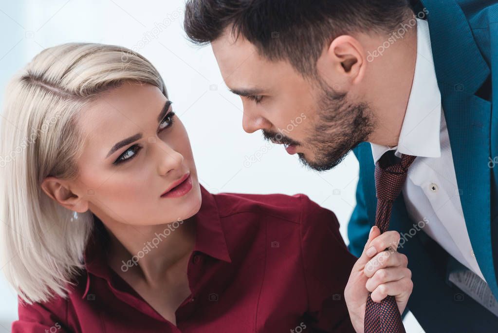 young business people looking at each other while businesswoman holding necktie of handsome businessman