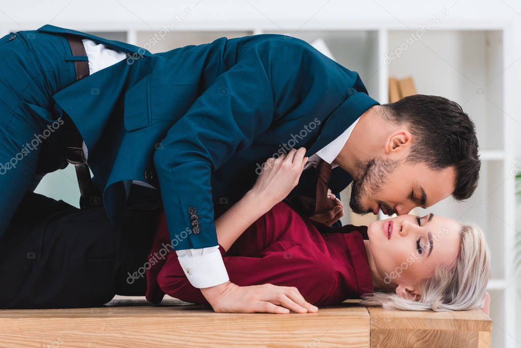 side view of sexy young couple kissing on table in office