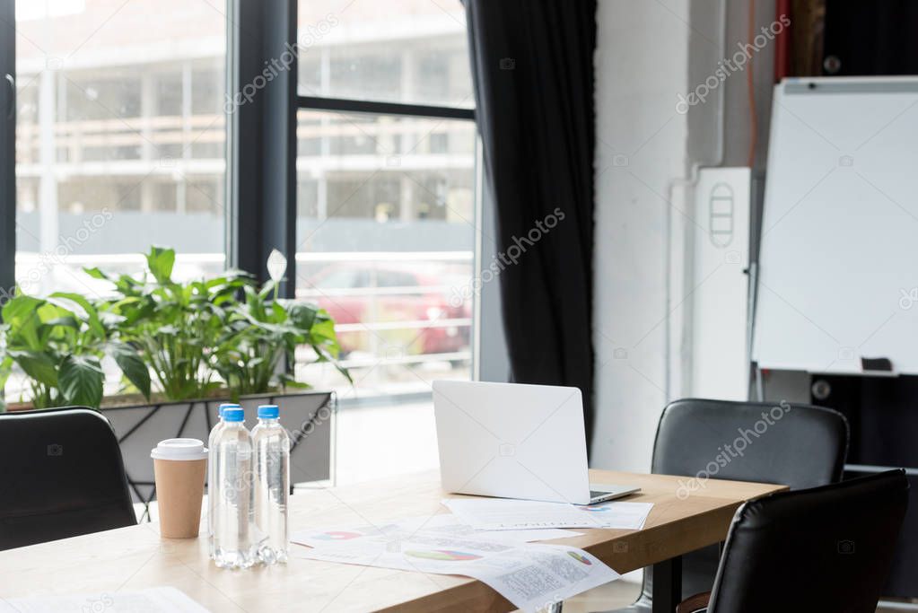 laptop, papers and bottles of water on table in modern office